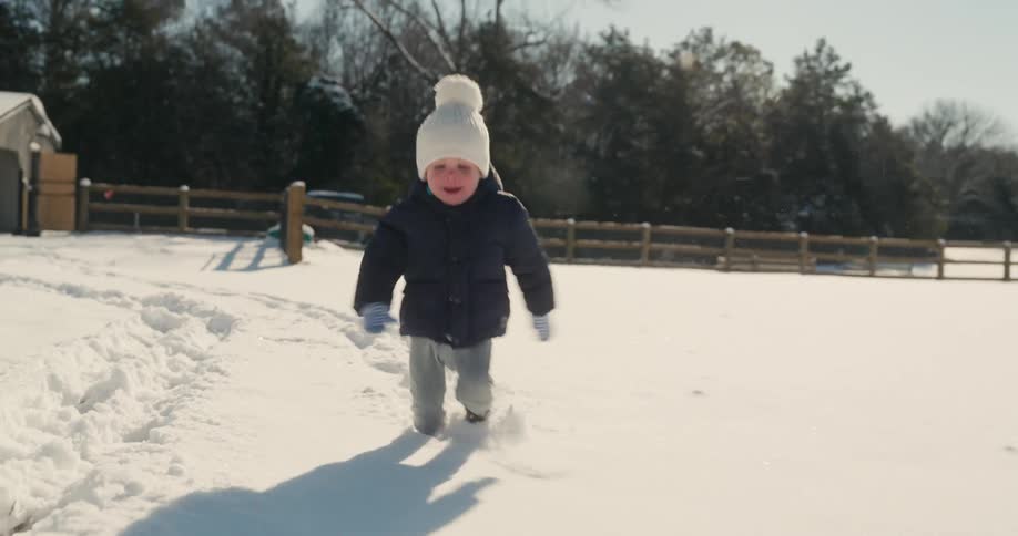 Child walks in the snow in a rural area surrounded by a wooden fence