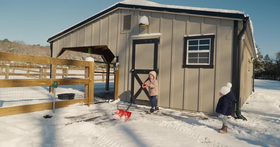 Girl shoveling snow in front of her house as her little brother looks around