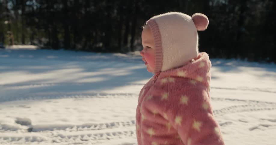 Child in pink winter outfit walks in the snow