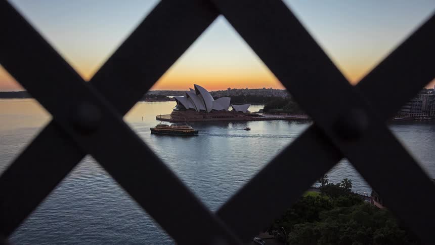 Boats drive around the harbor near the sydney opera house at sunset