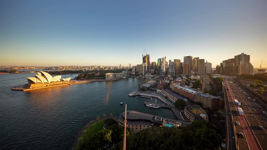 Traffic moves on freeways in and out of downtown as towers and skyscrapers overlook boats sailing off the coast and by the sydney opera house