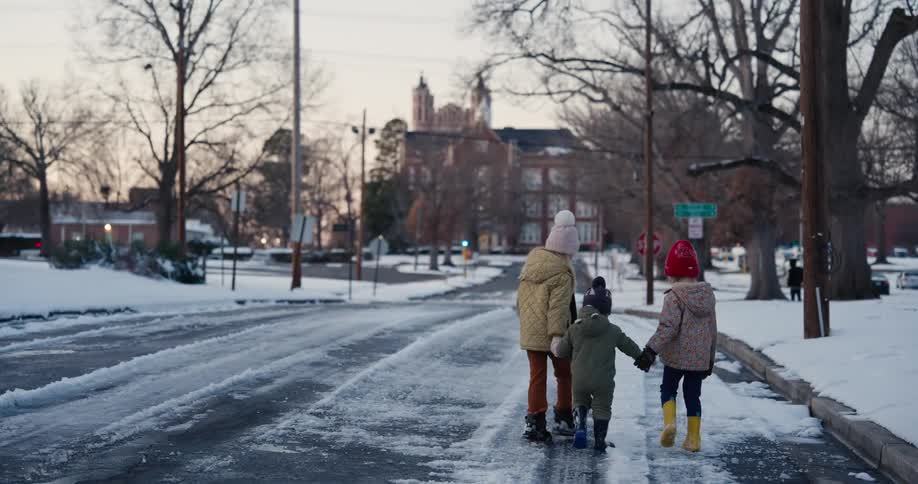 Three young girls hold hands while walking along a snow covered street