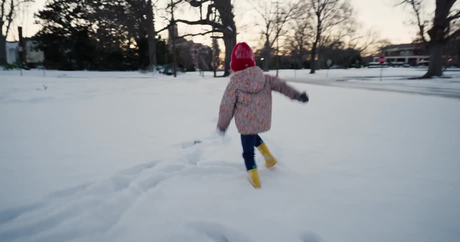 Little girl wearing a red beanie running in the snow in a residential area