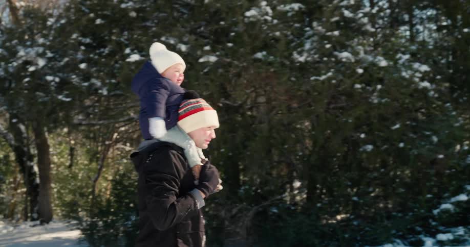Man walking in the snow with a child sitting on his shoulders in a wooded area
