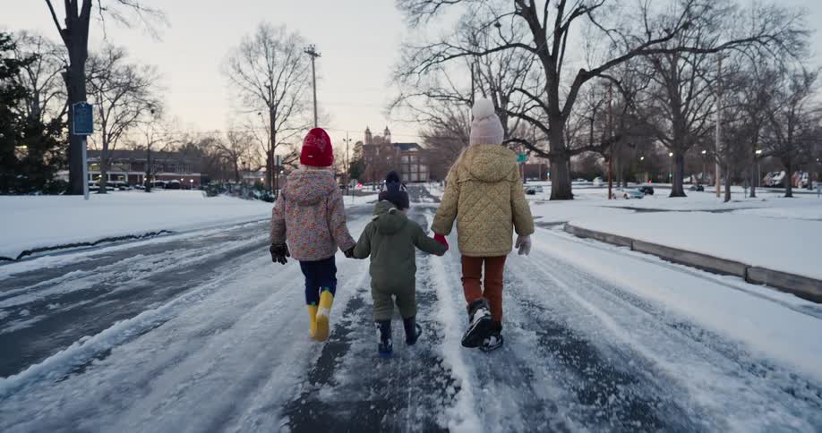 Three children holding hands walking on a snowcovered street at dusk
