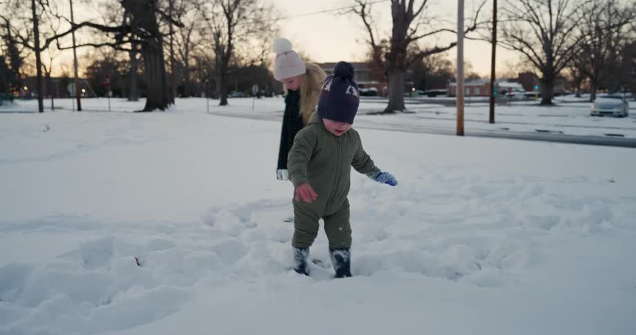 Two children walking and playing in the snow at a park at dusk