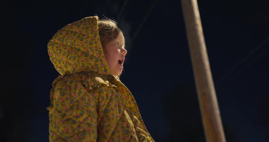 Little girl wearing a floral hooded coat under a streetlight at night