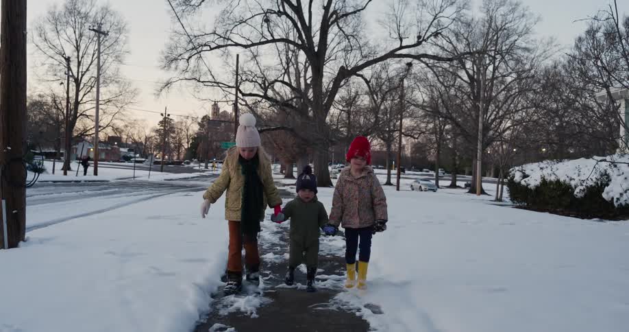 Three young girls slowly walk along a snow covered sidewalk