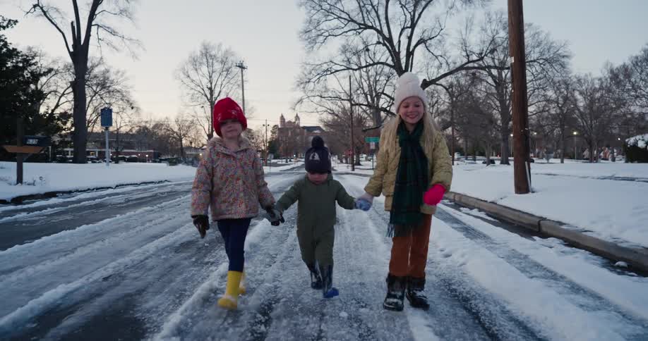 Three children walking down a street covered in snow