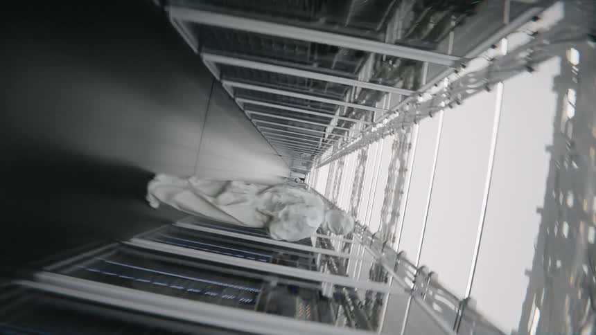 A worker wearing a white protective suit stands between long rows of server racks in a bright data center while the camera rotates rapidly down the central hallway