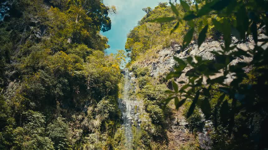 Waterfall flows down a cliff topped with trees with their autumn foliage on a cloudy fall day