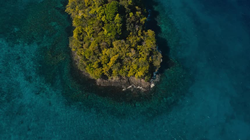 An overhead view shows a small island covered in green trees surrounded by deep blue ocean water