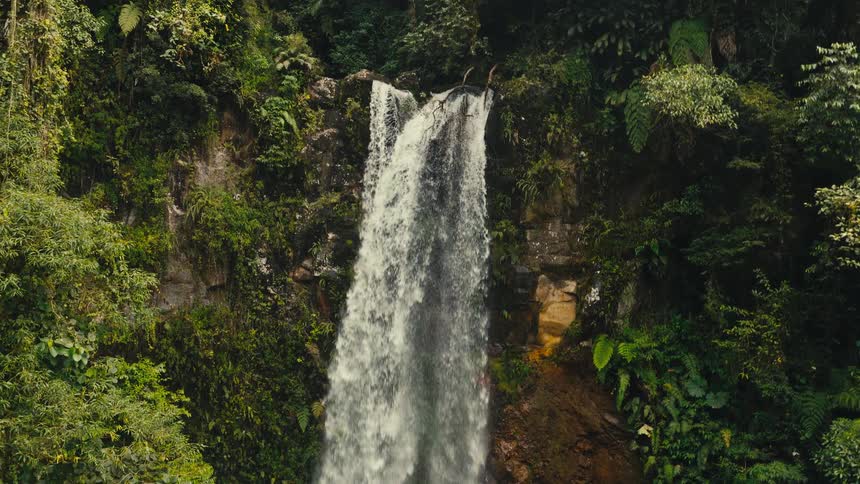 Waterfall on the ledge of a mountain surrounded by a dense forest area outdoros during day time