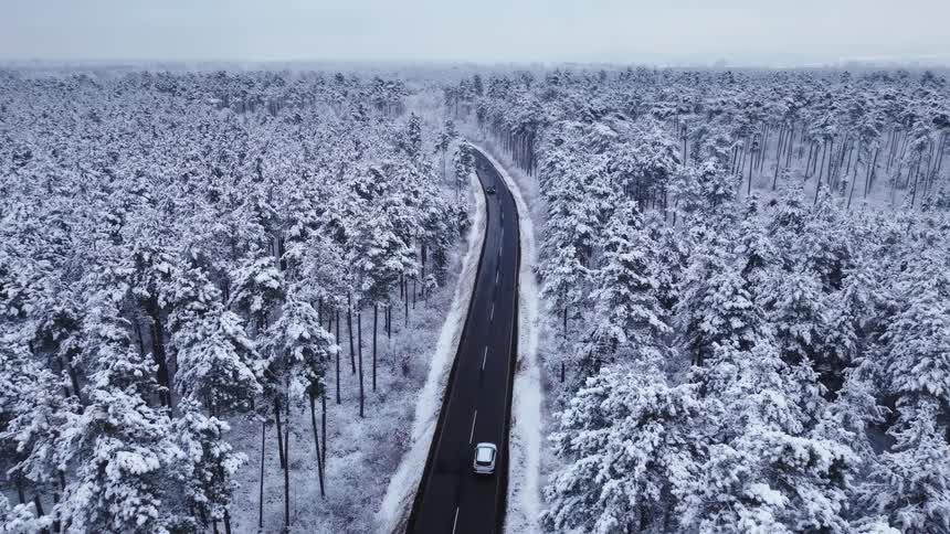 Car driving along a road surrounded by a snowcovered forest seen from above
