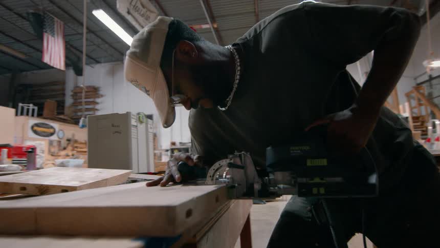 Man uses power tool to work on wood on workbench in workshop
