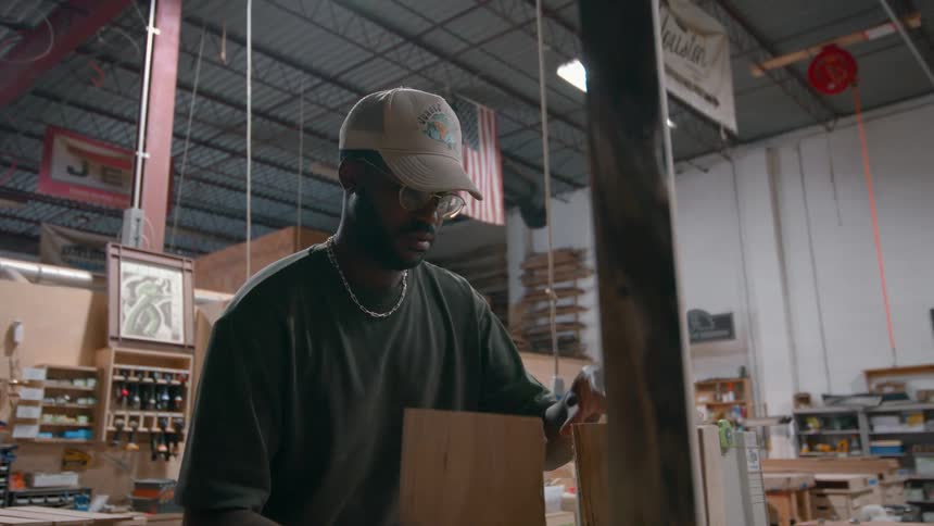 Man holds wooden piece vertically in workshop with industrial lighting