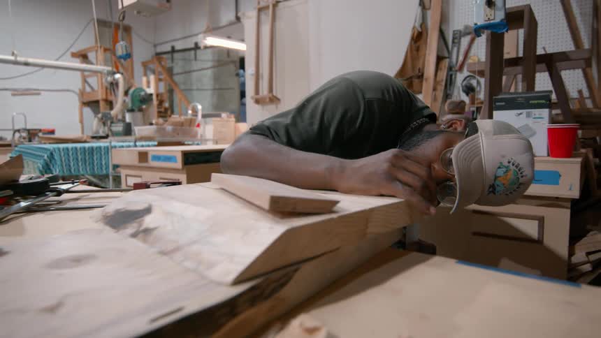Man bending over measuring a piece of wood as he works