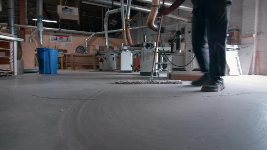 Man mopping the floor of a workshop with machines in the background