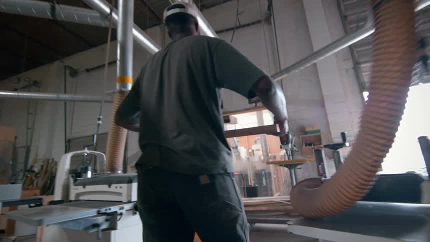 Worker carries multiple wooden squares during the daytime while in a workshop