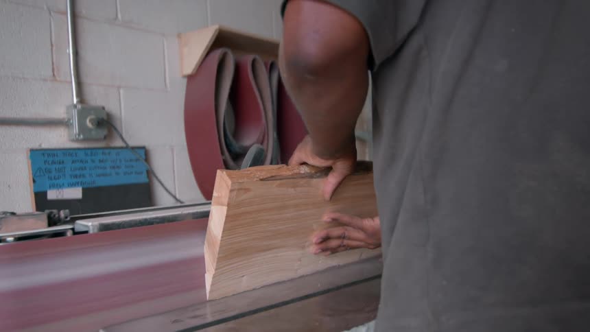 A male carpenter wearing glasses and a hat files a piece of wood using a filing machine