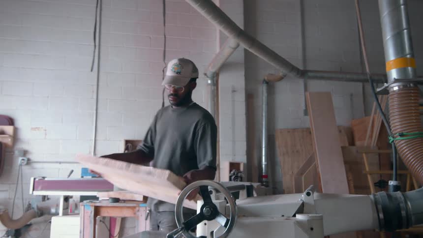 Man works with a thick square of wood using the machines in a workshop