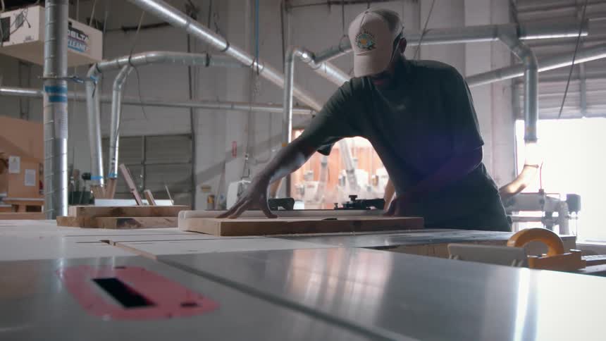 Man positions wooden board on saw in workshop with overhead ventilation system