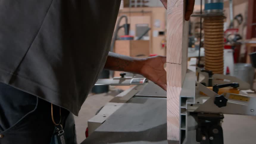 A black man saws a block of wood in a carpentry shop