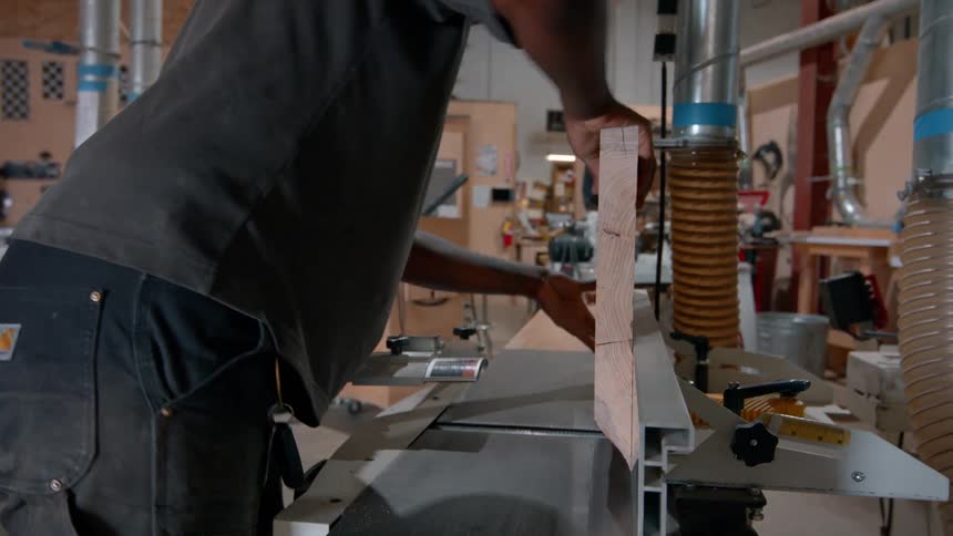 Man positions wooden piece on cutting machine inside carpentry workshop