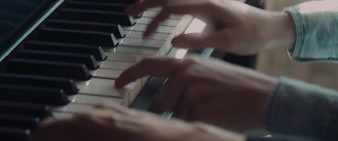 Hands play piano keys indoors