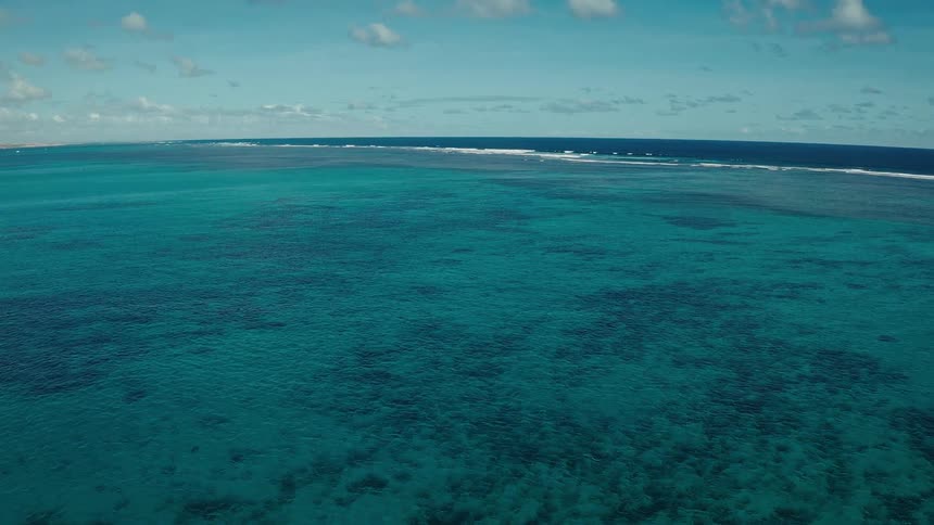 A subtle horizontal shift in the foreground and middle ground where the vibrant turquoise water meets the deeper navy blue this indicates the edge of the coral reef structure beneath the surface