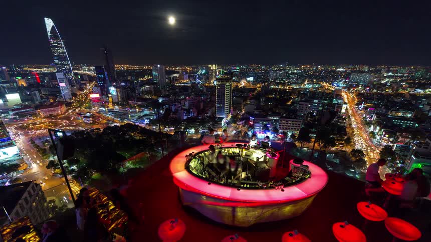 Rooftop bar overlooking illuminated city at night with moon in the sky