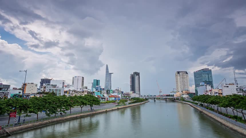 Urban canal surrounded by tall buildings and trees under cloudy sky