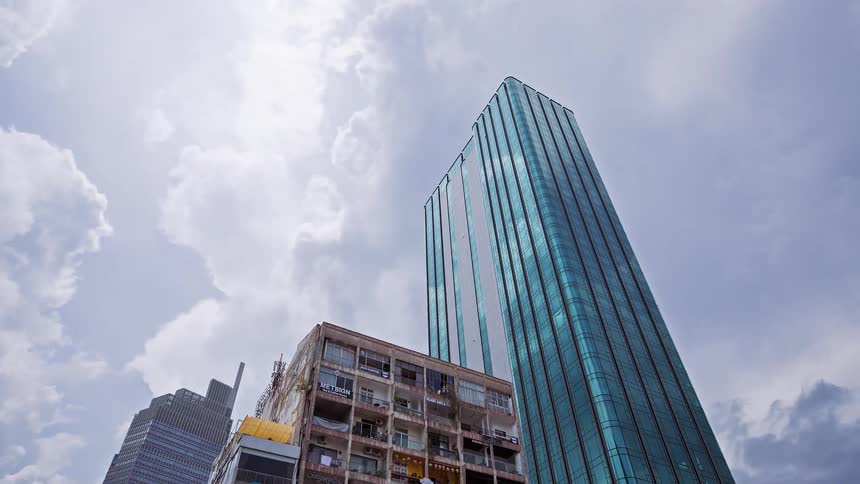 Modern glass skyscraper next to an old apartment building as clouds move across the sky and reflect on the glass tower windows
