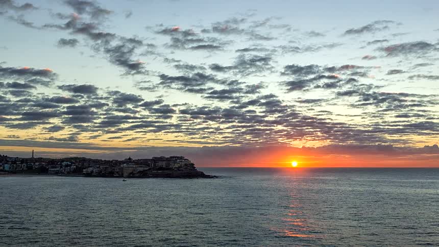 A city overlooking the ocean with an orange sun setting in the distance