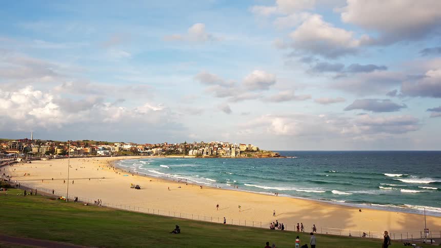 Town on the coast with buildings close together as people walk on the beach and waves roll in to shore