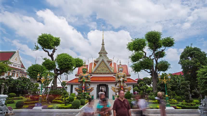 Temple with ornate central spire side statues and visitors in the garden under partly cloudy sky
