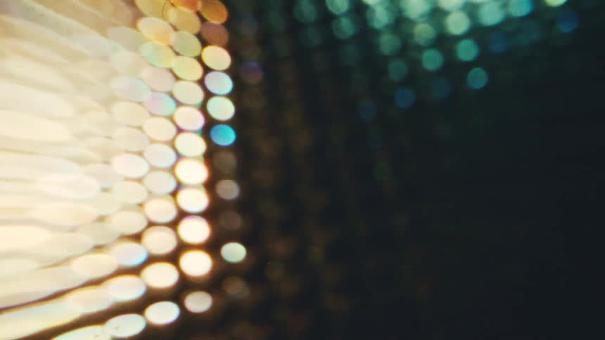 A close view shows a pattern of bright circular lights in warm gold and cool blue tones that shift out of focus against a dark background creating a soft glowing bokeh effect