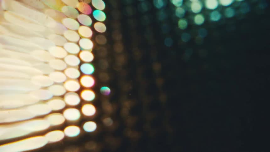 A close view shows a pattern of bright circular lights in warm gold and cool blue tones that shift out of focus against a dark background creating a soft glowing bokeh effect