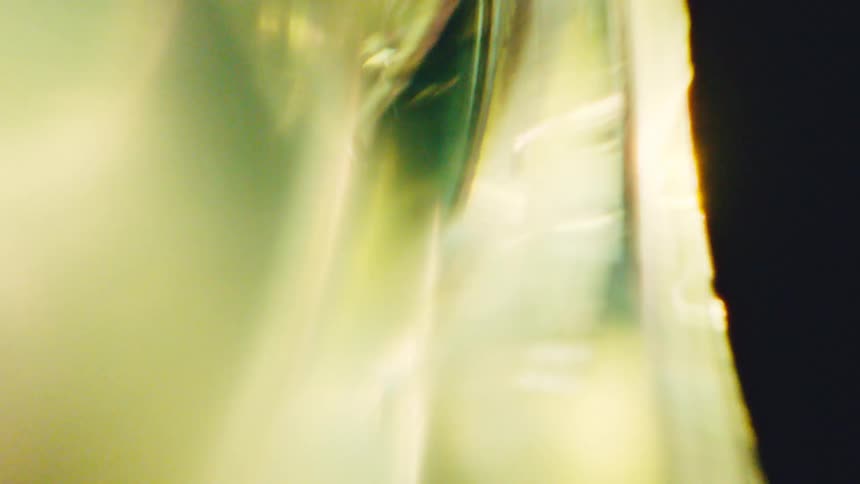 A close view shows a bright white curved light and soft golden glares that move across a dark black background creating an abstract glowing effect