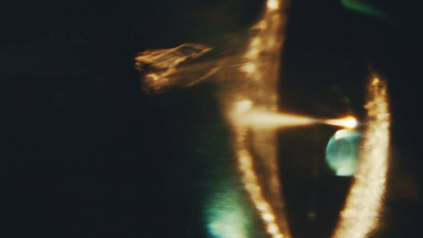 A close view shows a bright white curved light and soft golden glares that move across a dark black background creating an abstract glowing effect