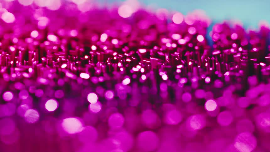 A close view shows small metallic pins that transition from a bright pink color to a cool blue as light reflects off the tops and creates a soft glowing bokeh effect against a dark background