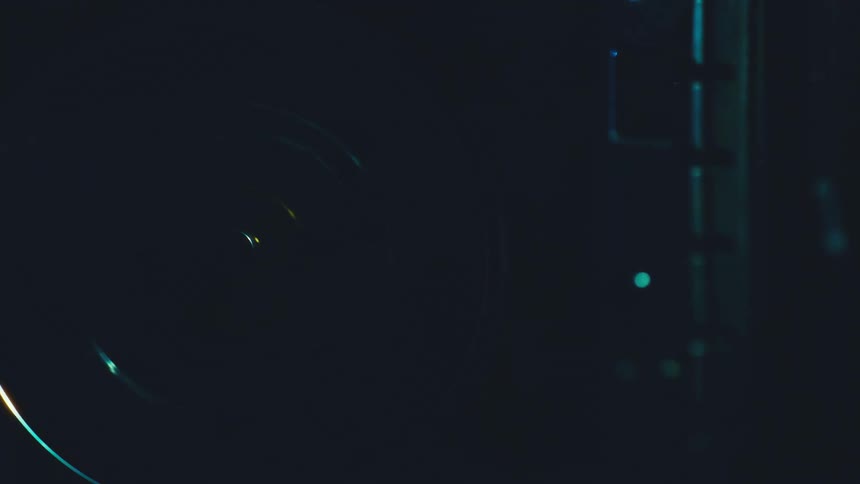 Circular metal disc illuminated in bluish tones beside industrial structure