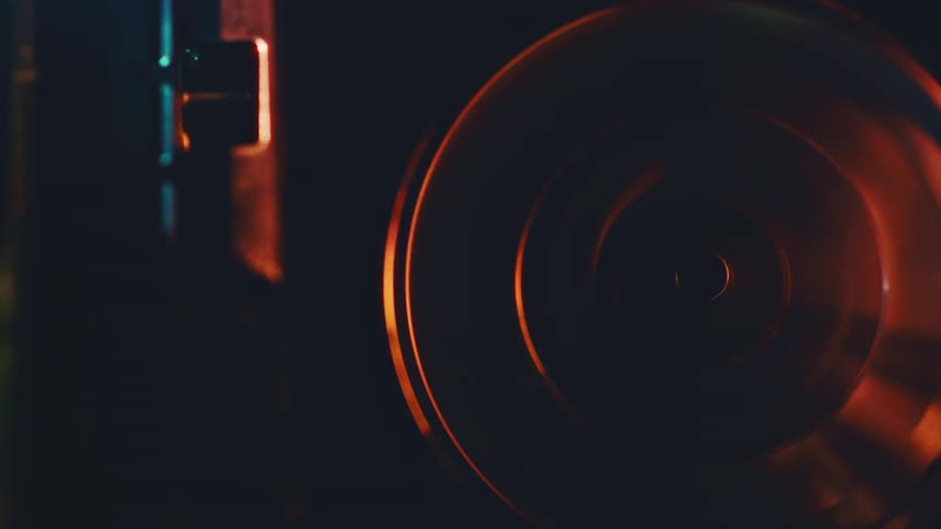 A close view of a large silver reel spinning in a dark room with subtle orange and blue light reflections on the metallic surface