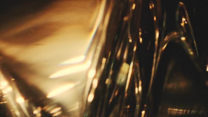 A close view shows warm golden light reflecting and shimmering through a textured glass surface against a dark background creating abstract shapes and bright flares