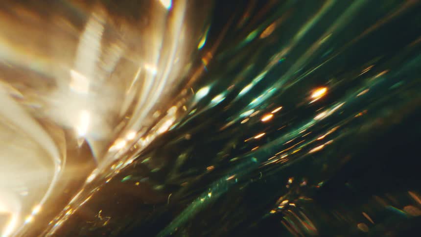 A dynamic interplay of light refracting through a crystalline or glasslike surface creating sharp streaks and bokeh effects the color palette is dominated by deep teals and warm amber tones giving the abstract movement a rich cinematic texture