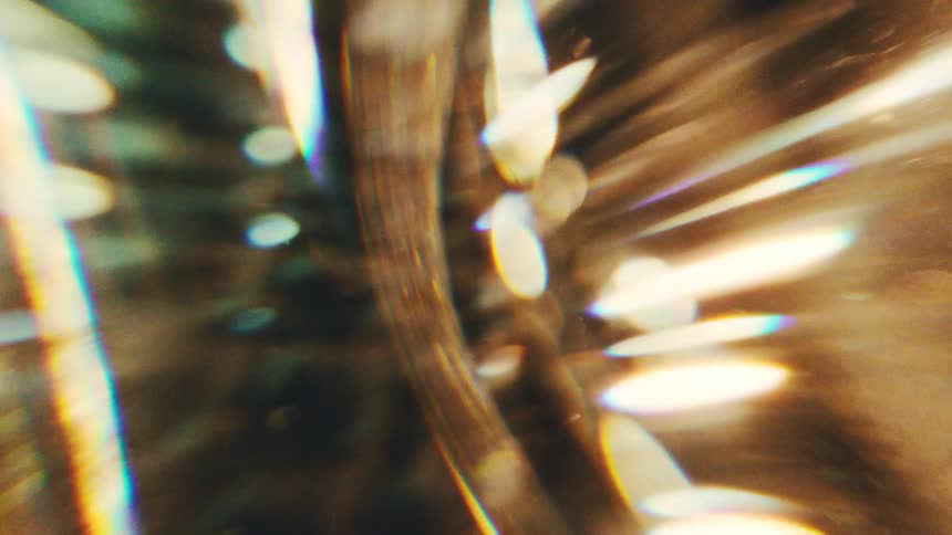Golden light leaks and prism flares moving across frame against dark out of focus background