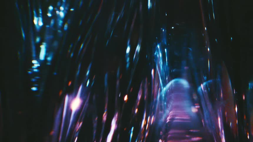 A close view shows bright blue and white light reflecting through textured glass with soft purple and orange glares moving across a dark background