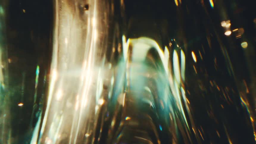A close view shows warm golden light and cool blue reflections shimmering through textured glass creating abstract moving shapes and bright flares against a dark background