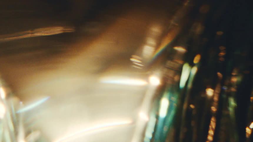 A close view shows warm golden light and cool blue reflections shimmering through textured glass creating abstract moving shapes and bright flares against a dark background