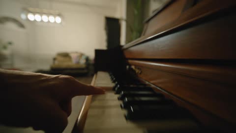 A persons hand plays a grand piano indoors striking the keys from left to right and then from right to left